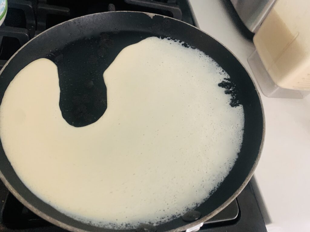 Crepe batter being tilted around a crepe pan, not all the way around yet, as a small part of the pan still does not have batter on it.