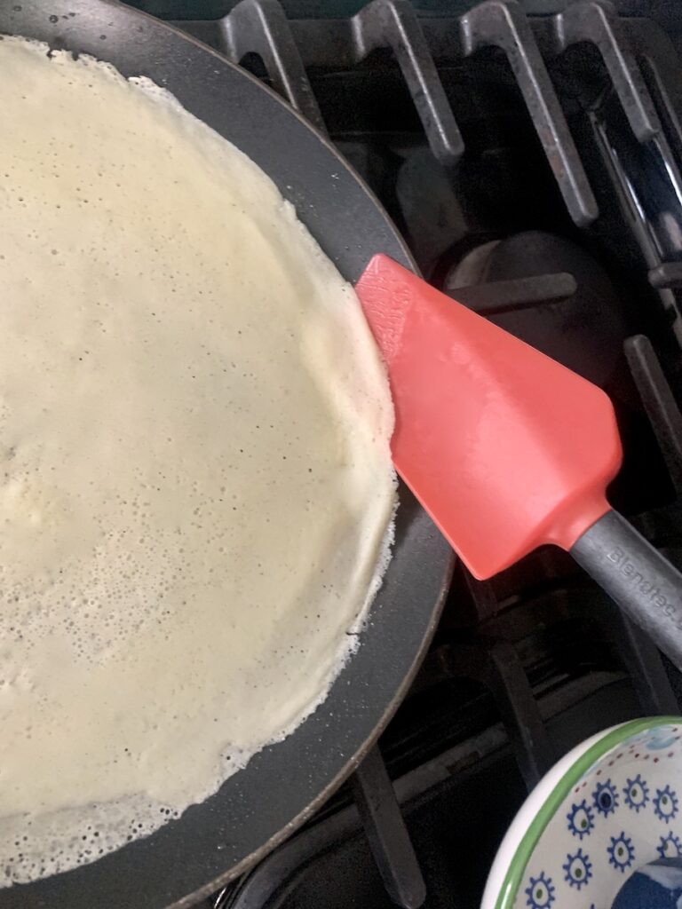 A red spatula releasing the edge of a crepe from the pan.