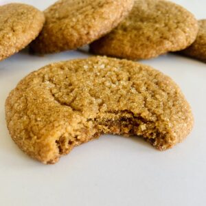 Gluten-Free gingersnap cookie with a bite missing. 4 more gingersnaps in the background.