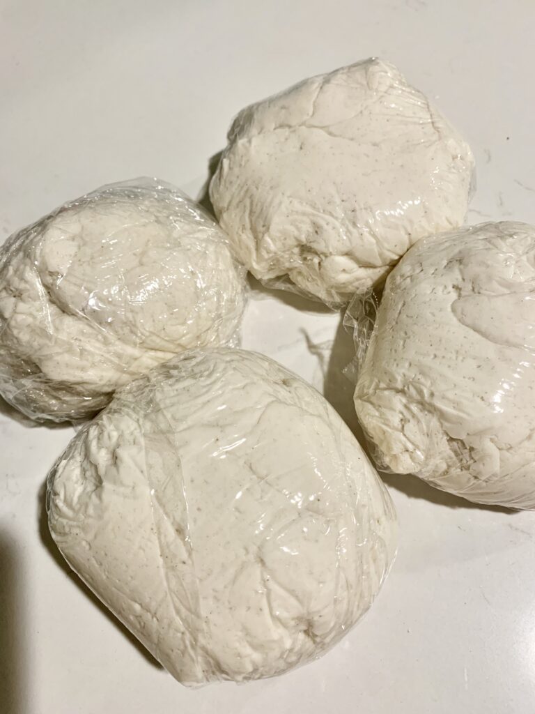 four balls of Caputo Fioreglut gluten-free flour pizza dough balls wrapped in plastic wrap