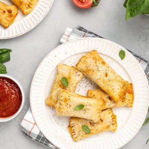 five gluten-free pizza pockets on a white plate, set on a table with a napkin and marinara dipping sauce
