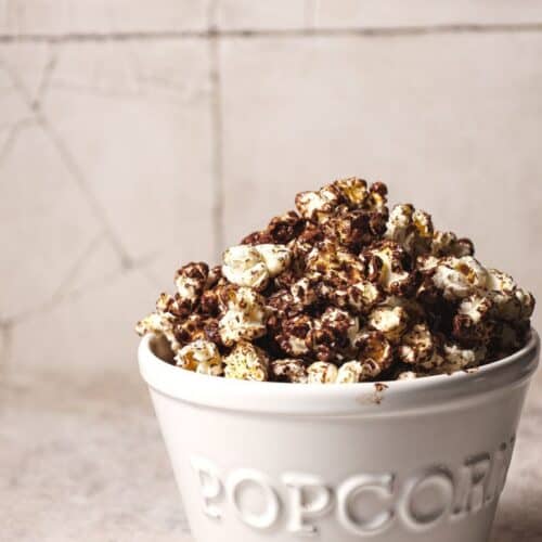 white bowl with text (popcorn) filled with chocolate covered popcorn