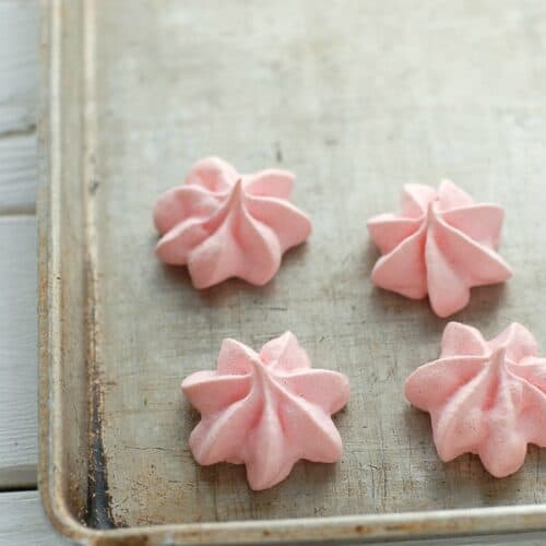 four star shaped pink merengues on a baking sheet
