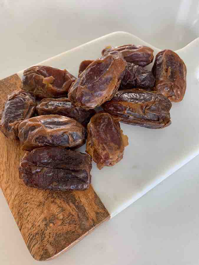 a pile of large medjool dates sitting on a wood & marble cutting board