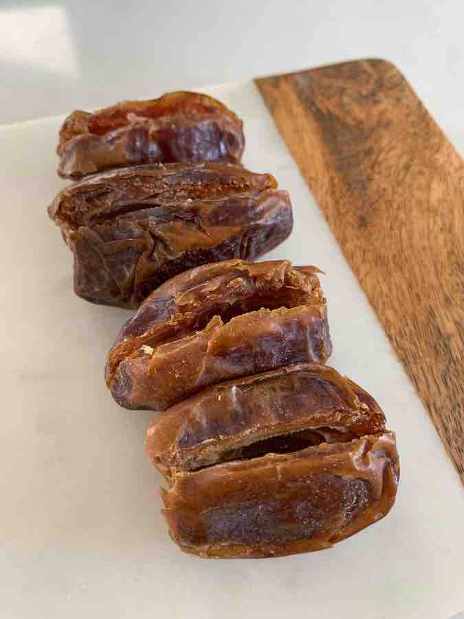 four opened Medjool dates, sitting in a row on a wood & marble cutting board