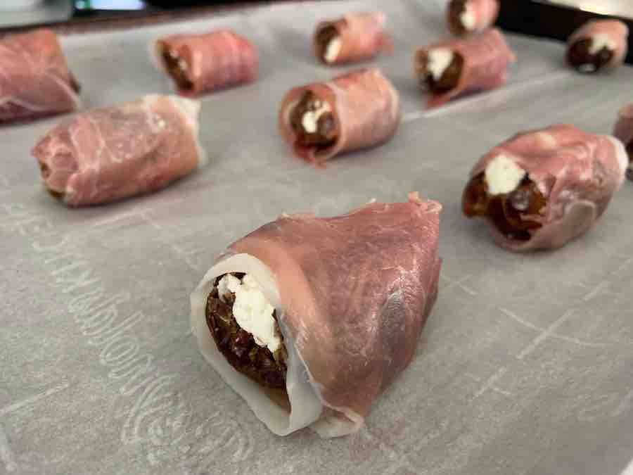 uncooked prosciutto-wrapped dates stuffed with goat cheese, sitting on a baking sheet lined with parchment paper