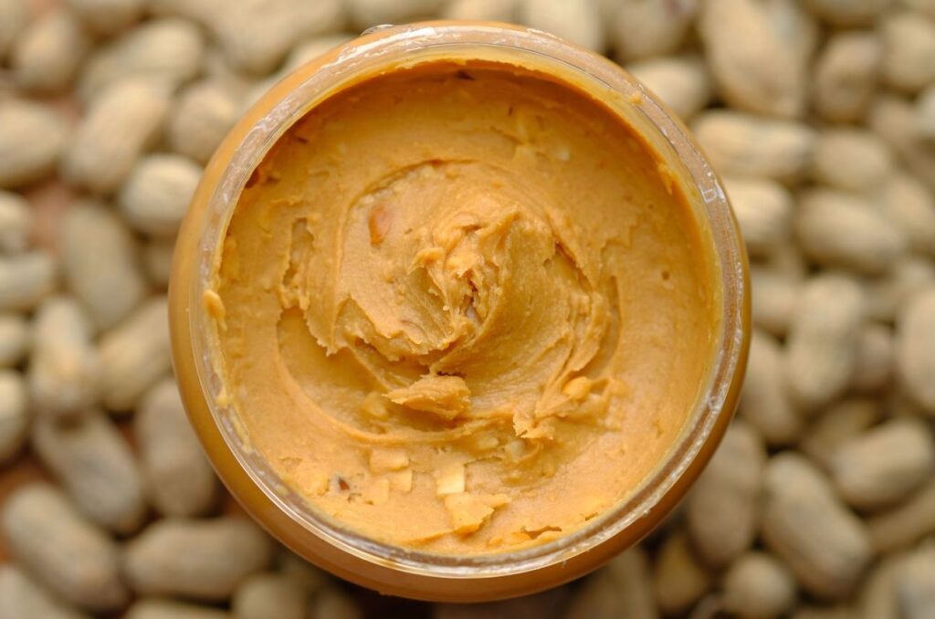 an open jar of peanut butter, viewed from above, in the middle of a pile of peanuts with shells