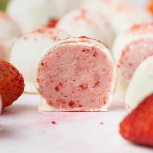 pink-inside view of a cut open strawberry truffle, whole truffles and strawberries in background