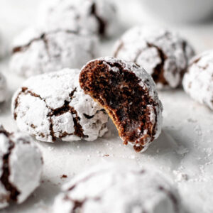 chocolate cookies with white powdered sugar exterior on a counter, one is opened to reveal chocolate inside