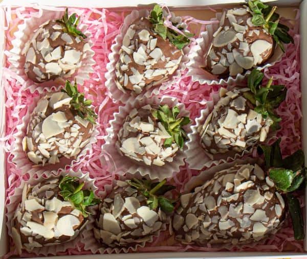 a box of gluten-free chocolate-covered strawberries covered in nuts on white wrappers and pink filling