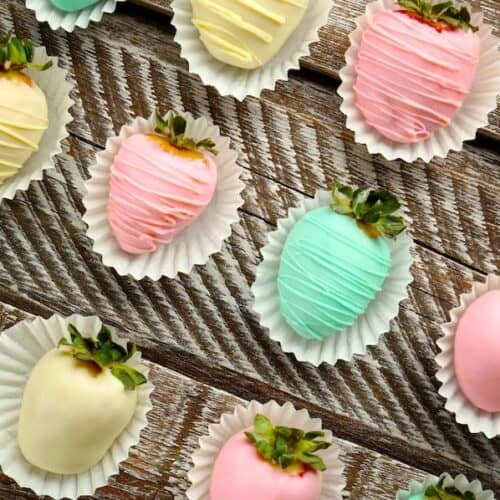 pastel white-chocolate covered strawberries (green, yellow and pink) on white candy wrappers in rows on a wooden table