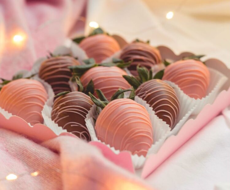 milk chocolate and pink chocolate-covered strawberries in a pink box, fairy lights