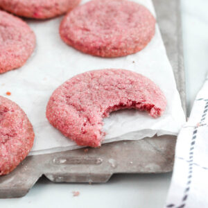 pink cookies on white paper, one with a bite missing