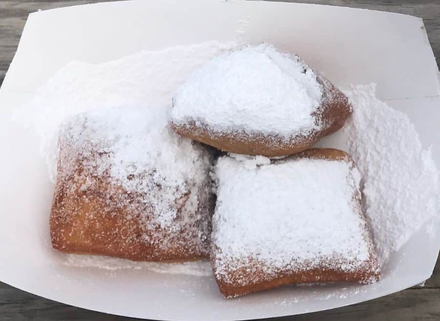 3 beignets covered with powdered sugar in a to-go tray