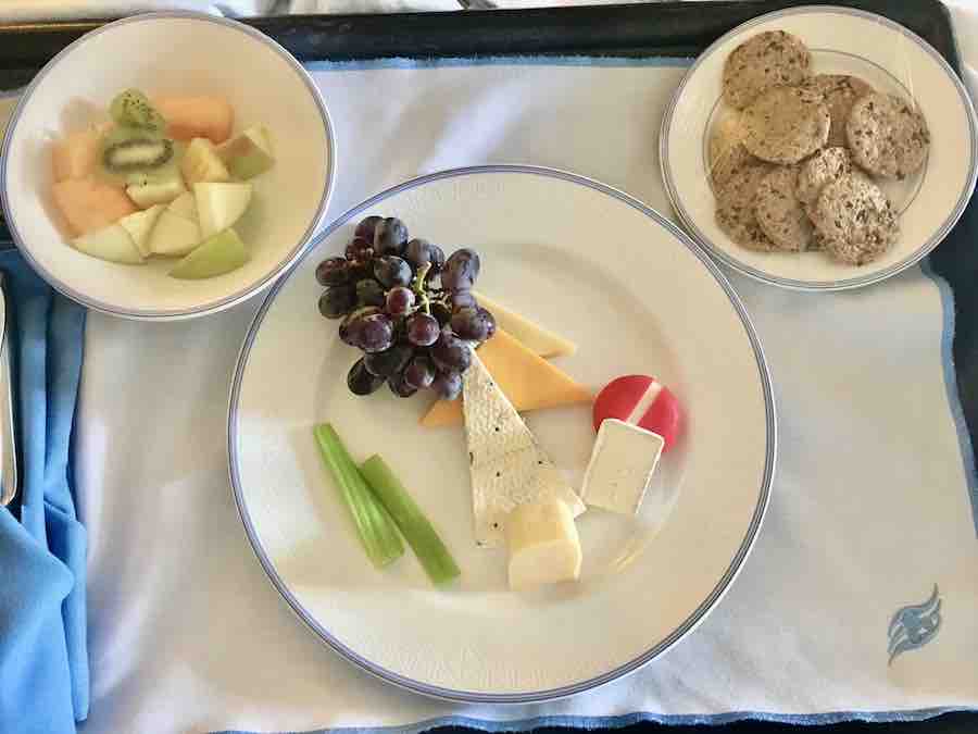 room service on.a tray with 3 plates in a Mickey Mouse head shape.... large center plate has celery, grapes & a variety of cheeses, left ear has sliced fruit, right ear has gluten-free crackers