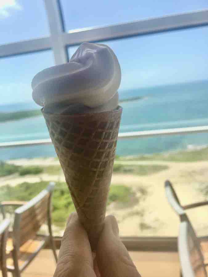 soft service ice cream in a gluten-free ice cream cone, ocean and sand & balcony railing in the background