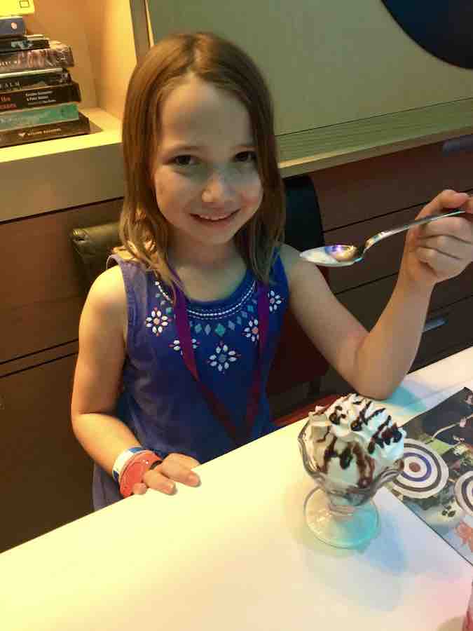 Miss E smiling holding a spoon eating a gluten-free ice cream sundae