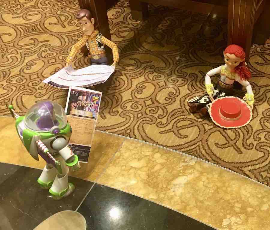 Buzz, Woody and Jessie toys set up like they are hanging out on the cruise ship... Buzz is standing & looking at a brochure, Woody is seated looking at a program, and Jessie is sitting with her hat off