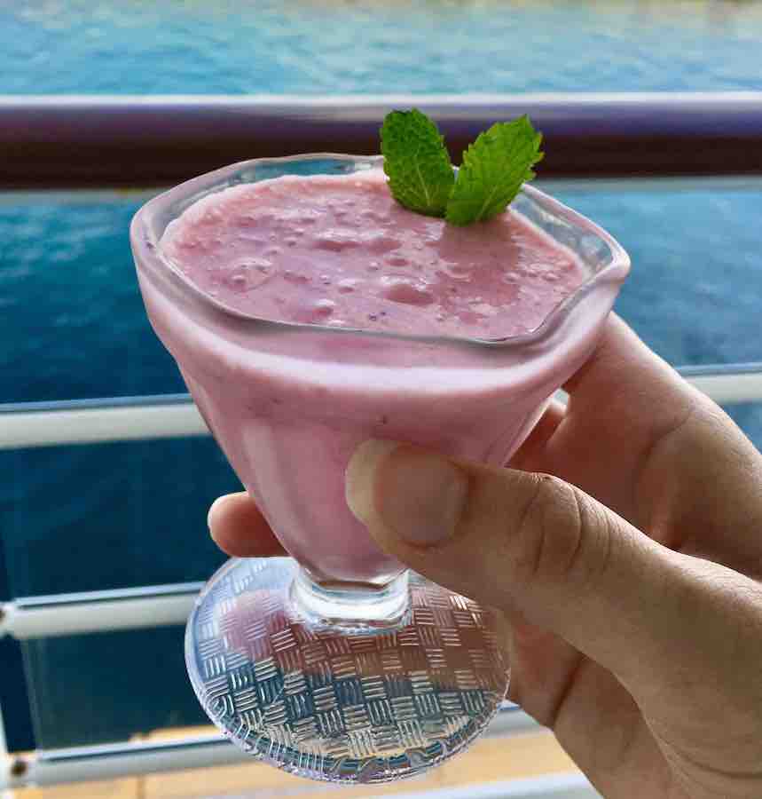 a berry smooth with a few mint leaves, held in a hand, with the ocean and cruise ship balcony in the background