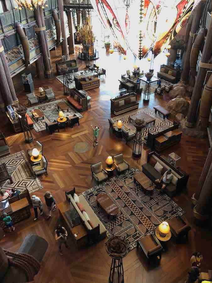 giant lobby of Animal Kingdom Lodge, chandelier, sofas & seating groups, and very small in the middle is CJ with arms outstretched and Mickey ears