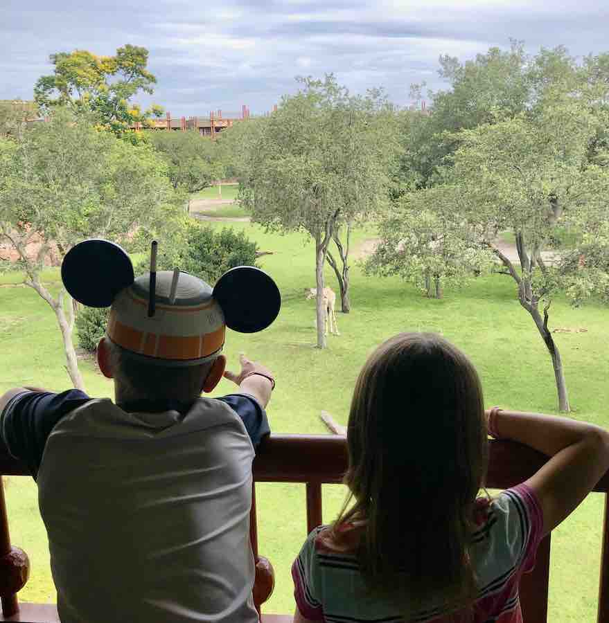 silhouettes of CJ with Mickey ears and Miss E looking off a balcony at a giraffe on the savanna