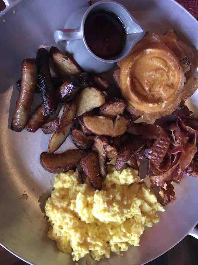 allergy skillet with gluten-free Stitch waffles, bacon, fried potatoes, sausage, eggs and a small pitcher of syrup