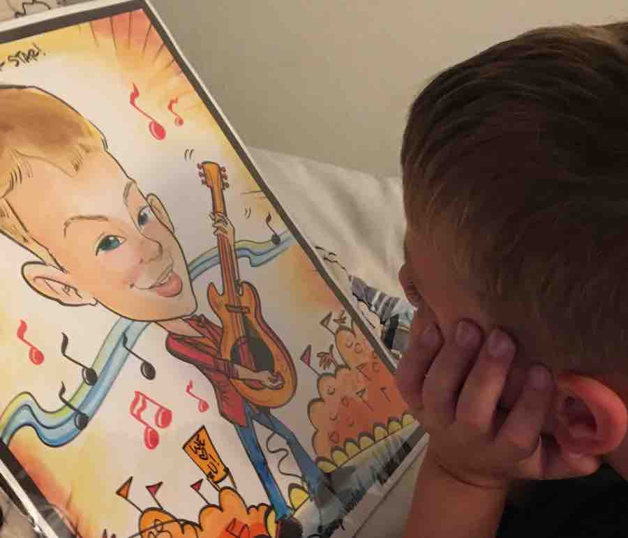 CJ with his hand on face, admiring the caricature of him playing a guitar