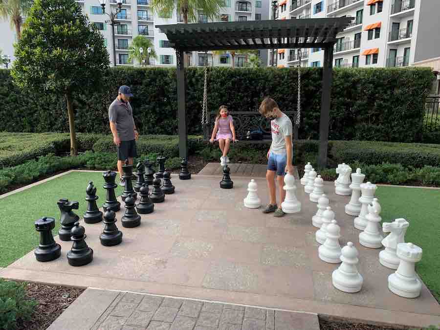 Dave & CJ playing with a very large chess, while Miss E watches from the bench swing