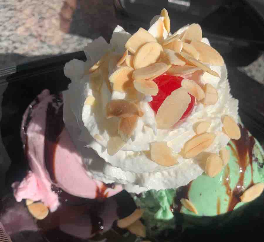 an ice cream sundae with strawberry and mint chip ice cream, topped with whipped cream, nuts and a cherry