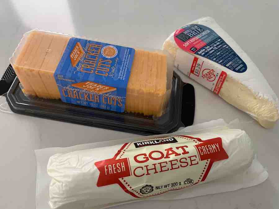 packages of cheddar, brie, and goat cheese on a white counter