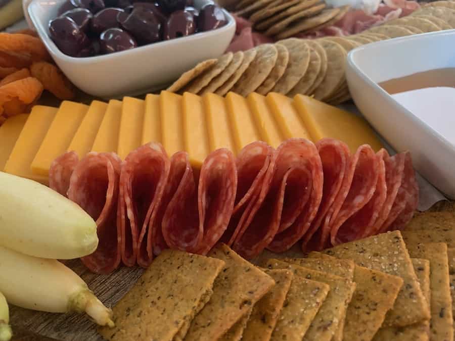close up of a gluten-free charcuterie board with crackers, sliced cheddar, salami, carrots, honey, andolives