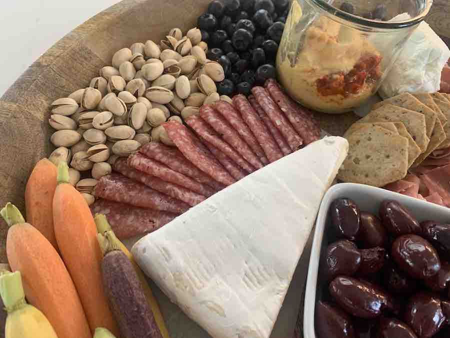 close up of a gluten-free charcuterie board with crackers, salami, carrots, pistachios, blueberries olives, hummus, and brie
