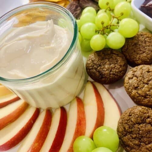 Caramel Cream Cheese dip on a platter with sliced red apples, green grapes, and brown mini muffins.