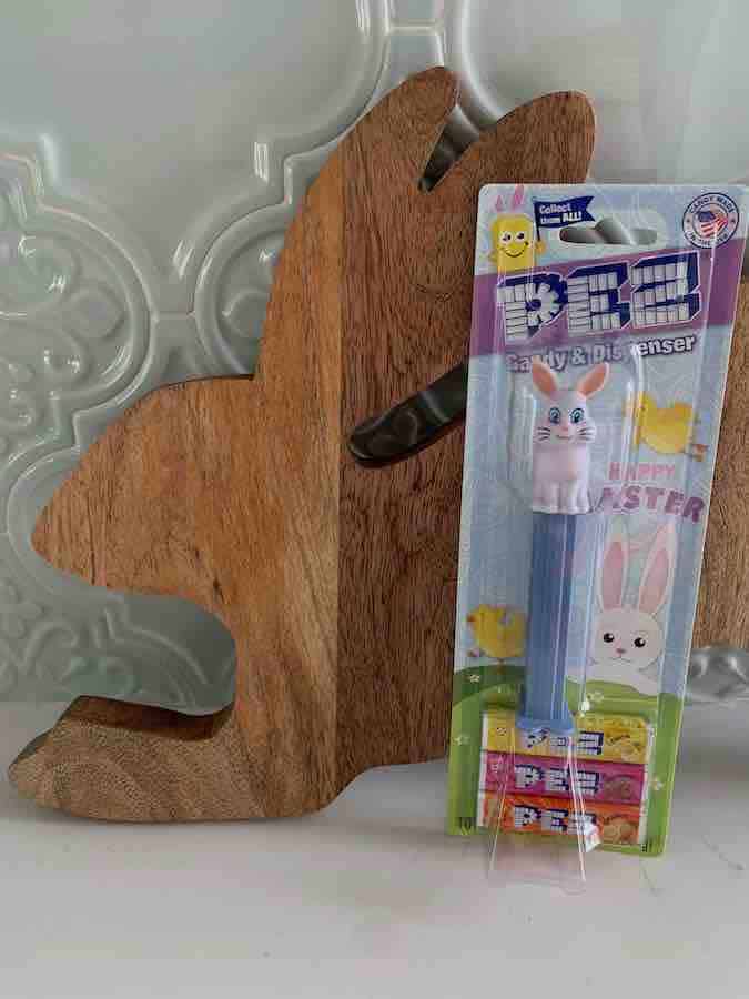 a package of a PEZ bunny dispenser & candy, in front of a wooden bunny cutting board