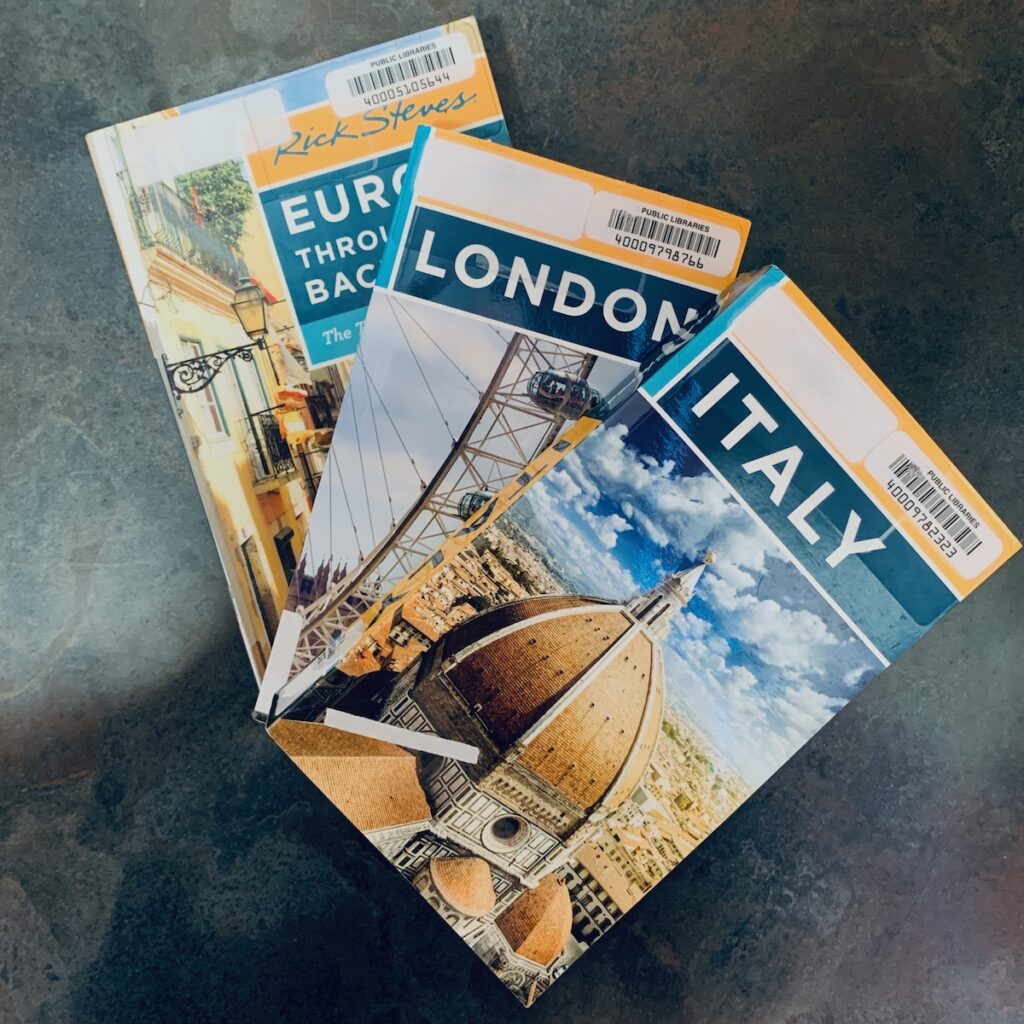 3 guidebooks on table for Italy, London, and Europe Through the Back Door.