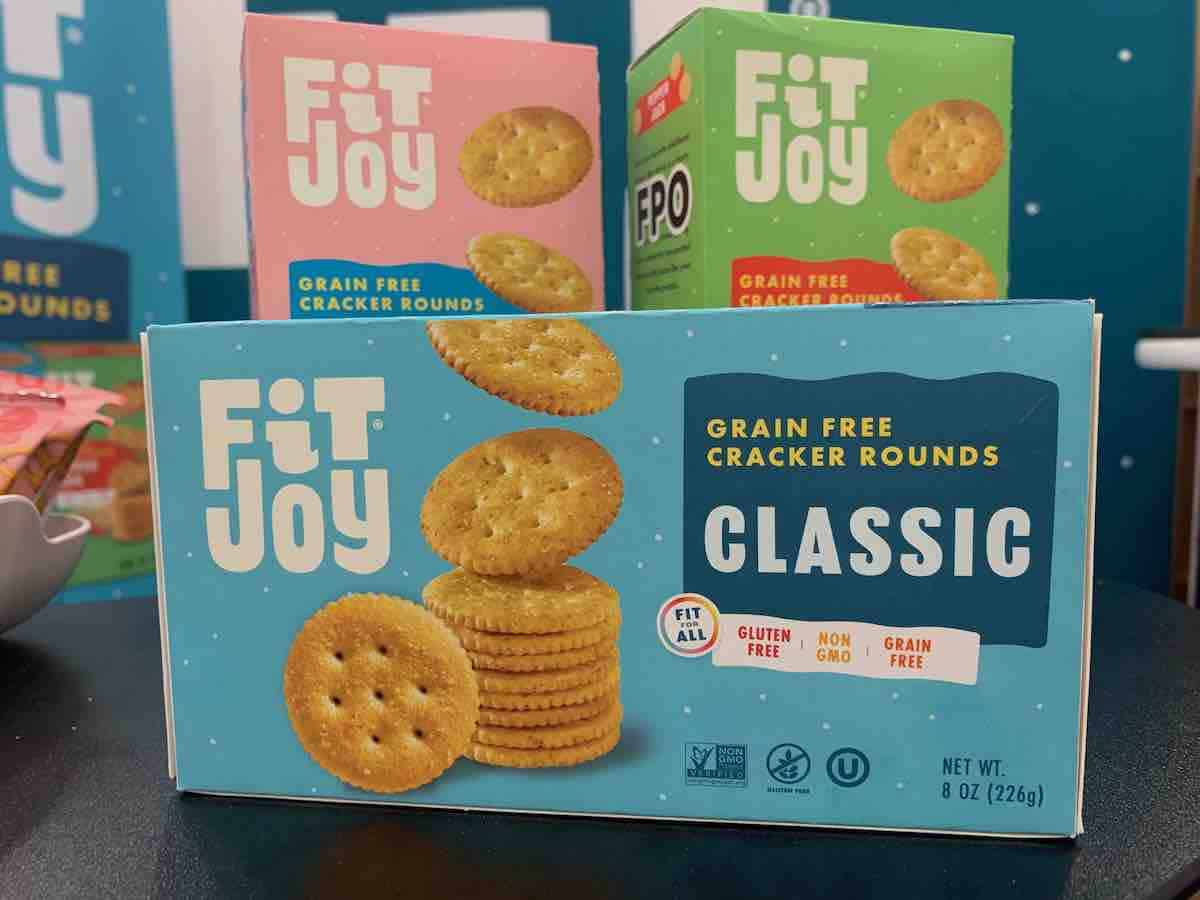 Package of gluten-free fit joy crackers (look like Ritz crackers), on a display table at Expo West with 2 more boxes in the background