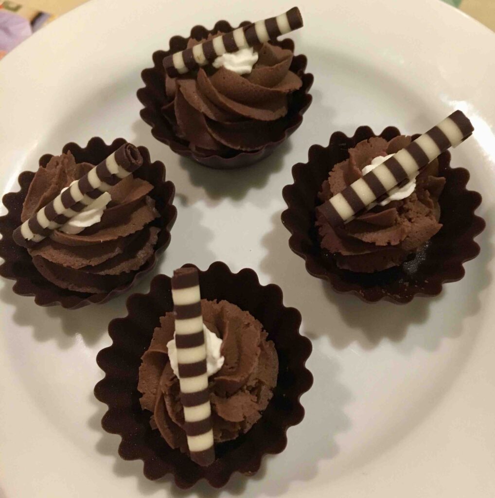 four small chocolate-style desserts with striped white & dark chocolate tubes on top