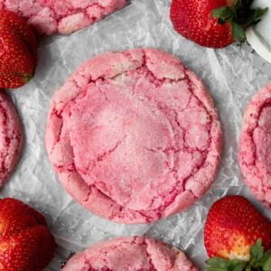 gluten-free strawberry sugar cookie on parchment paper, parts of more cookies and strawberries in the background