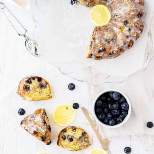 Gluten-Free Lemon bundt Cake With Blueberries.. a few slices are cut out of the bundt cake and on the counter, blueberries and lemon in photo for decoration