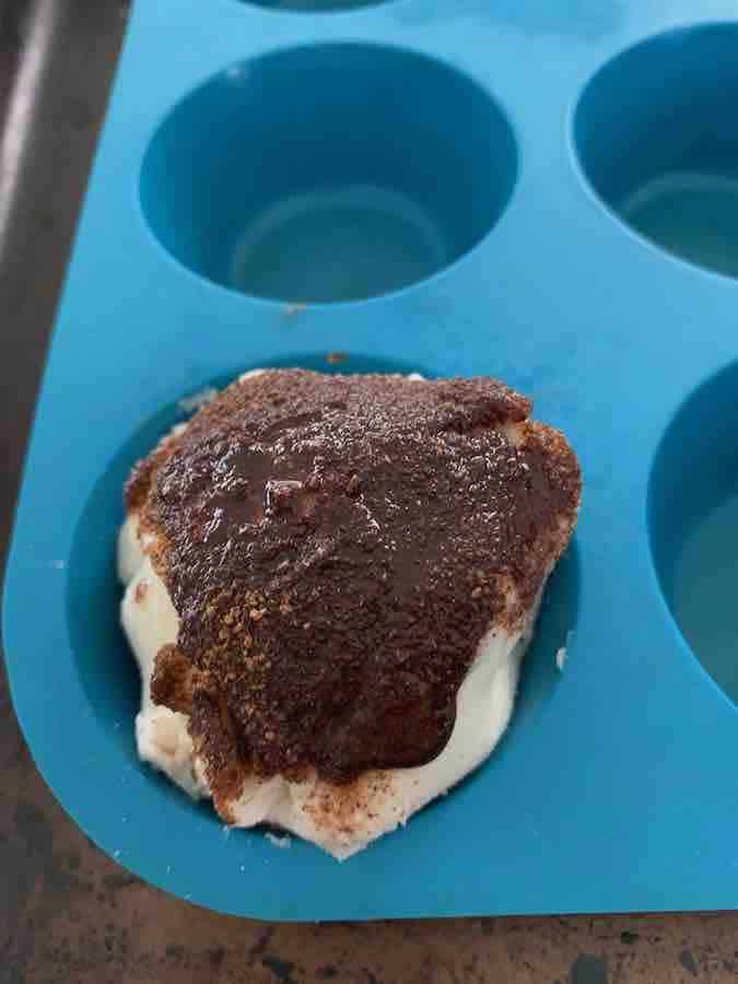 gluten-free resurrection roll(unbaked) with cinnamon topping visible, in a blue silicone muffin pan
