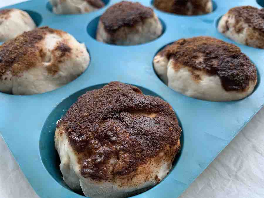 gluten-free resurrection rolls (unbaked) with cinnamon toppings visible, in a blue silicone muffin pan