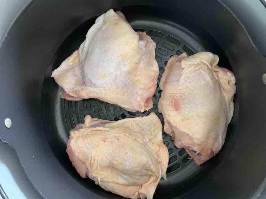 three raw chicken thighs spaced in an air fryer basket, with space for air to circulate
