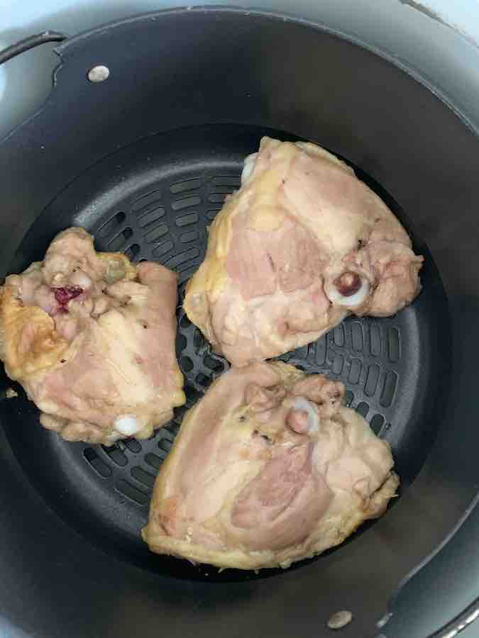 three 1/2 cooked chicken thighs (skin down) spaced in an air fryer basket, with space for air to circulate