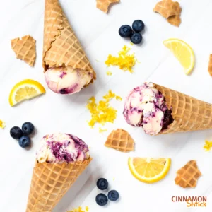 3 cones of Lemon Blueberry Ice Cream, lemon slices, blueberries, and cone pieces scattered all over a white counter