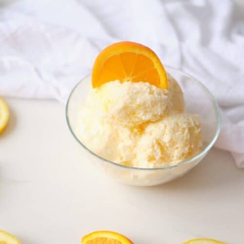 a bowl of Lemon Orange Ice Cream with a white napkin and orange and lemon slices scattered on the counter