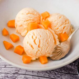 3 scoops of Melon Ice Cream in a white bowl with cut pieces of melon sprinkled around the ice cream