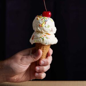 eggless, homemade vanilla ice cream, in a cone, with sprinkles and a cherry on top