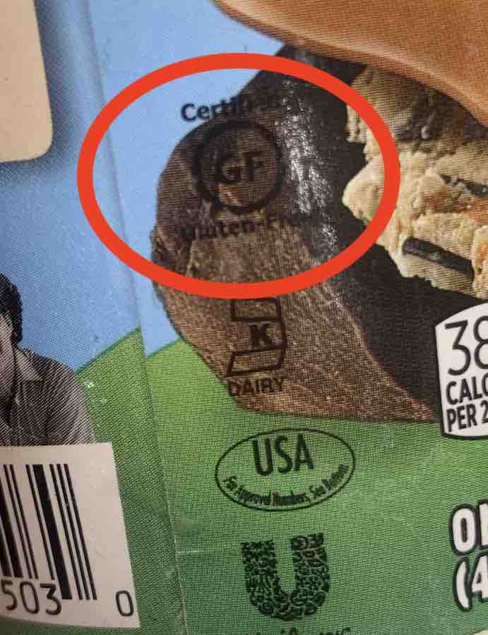 Ben & Jerry's pint, zoomed in on old-style gluten-free logo: a circle with "GF" in the center, "certified" above and "gluten-free" below.. the logo is in black print over an image of dark chocolate and barely visible, so it is circled in red 