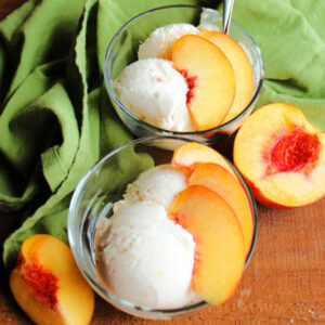4 Ingredient Peach Ice Cream in two bowls with peach slices on a table with a green napkin and a cut peach
