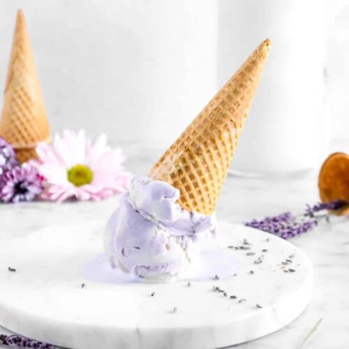 Homemade Lavender Ice Cream in an upside down cone on a round marble slab, lavender and flowers for decoration